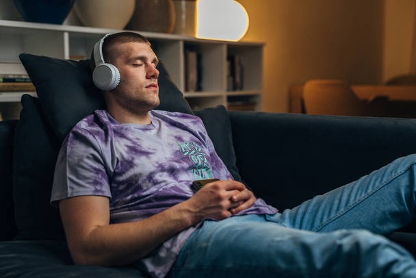 A tired caucasian man fell asleep while listening to music on the sofa. - Fotó, kép
