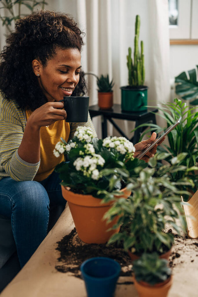 A beautiful multiracial woman is working with plants. She takes a break to enjoy coffee - Φωτογραφία, εικόνα