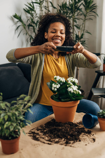 Mutlu kadın saksı bitkisinin fotoğrafını çekiyor. - Fotoğraf, Görsel
