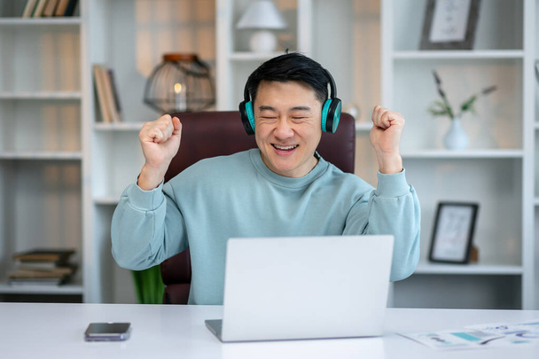 Šťastný uvolněný asijský muž nosit bezdrátové sluchátka dokončil práci poslech oblíbené hudby, baví během přestávky - Fotografie, Obrázek