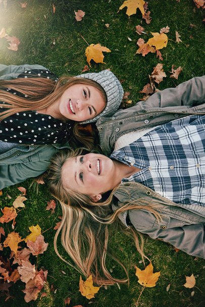 Dichtbij genoeg om zussen te zijn. Hoge hoek schot van twee gelukkige tieners ontspannen samen op het gras buiten - Foto, afbeelding