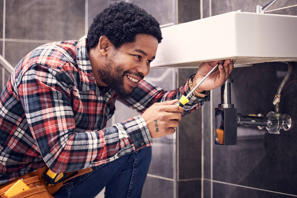 Happy, man or plumber fixing a sink with smile in maintenance or installation in home repairs. African handyman or worker with plumbing tools to fix water pipes or house basin in renovation project. - Zdjęcie, obraz
