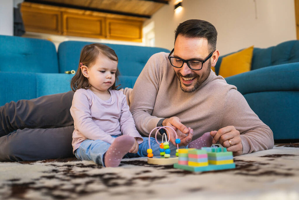 Ojciec i córka bawią się na podłodze w domu dojrzały dorosły mężczyzna kaukaski bawić się z jego dwuletnim dzieckiem dziewczynka o zabawy rodzicielstwo i więzi rodzinnego czasu pojęcie skopiować przestrzeń prawdziwi ludzie - Zdjęcie, obraz