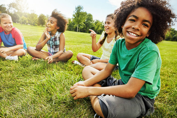 My friends are the coolest to hangout with. Portrait of a young boy sitting together with his friends on the grass outside - Fotoğraf, Görsel
