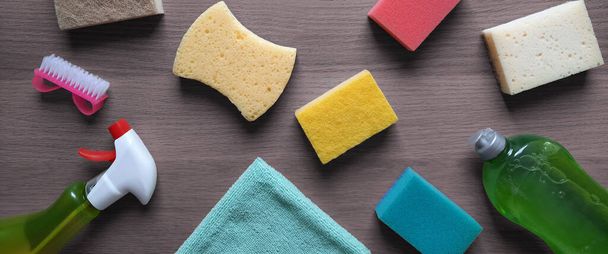 Banner for website with cleaning products. Flat styling. Kitchen sponges, washclothes, scrub-brushes, detergent liquid, cleaning spray lie on wooden table. Top view. Home cleaning service concept. - Foto, imagen