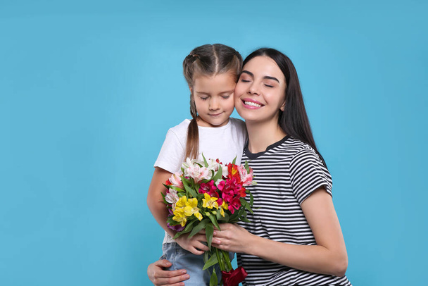 Happy woman with her daughter and bouquet of beautiful flowers on light blue background, space for text. Mother's day celebration - Foto, Imagem