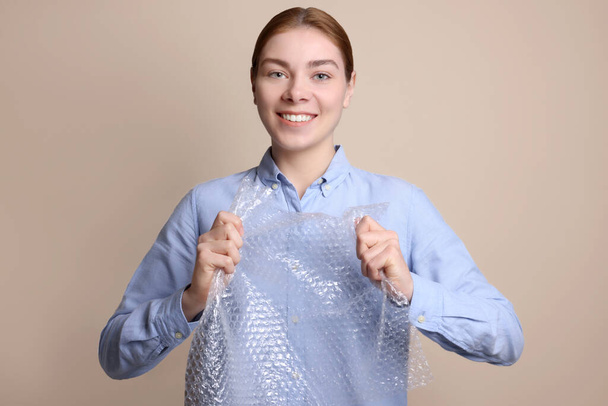 Woman popping bubble wrap on beige background. Stress relief - Foto, immagini
