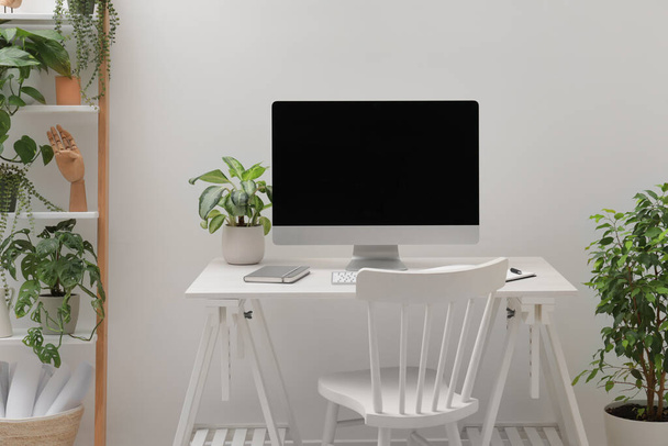 Tágas munkaterület íróasztallal, székkel, számítógéppel és cserepes növényekkel otthon - Fotó, kép