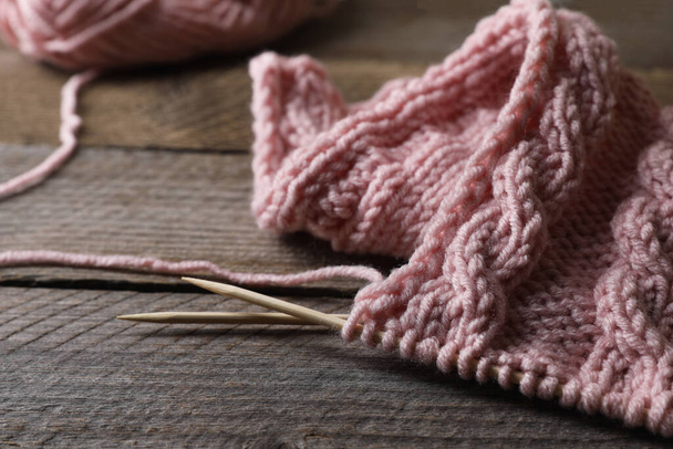 Pink knitting and needles on wooden table, closeup - Foto, afbeelding