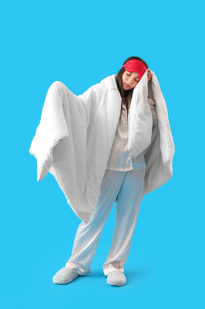 Young woman with sleeping mask and soft blanket on blue background - Foto, imagen