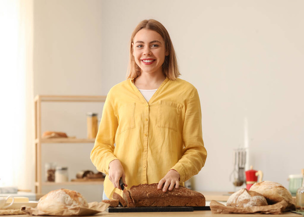 Молода жінка ріже свіжий хліб за столом на кухні
 - Фото, зображення