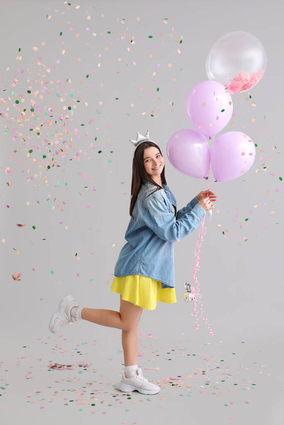 Glückliche junge Frau mit Luftballons feiert Geburtstag auf grauem Hintergrund - Foto, Bild