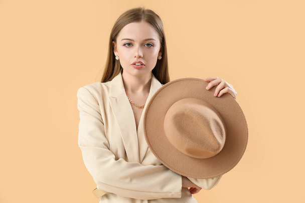 Modieuze jonge vrouw met hoed op beige achtergrond - Foto, afbeelding
