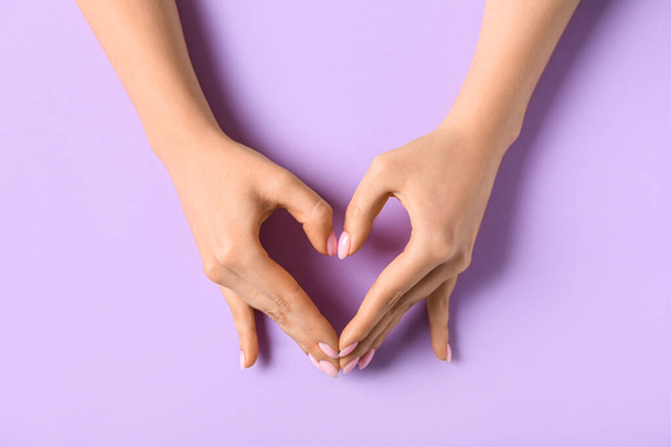 Mujer haciendo corazón con sus manos sobre fondo lila - Foto, Imagen