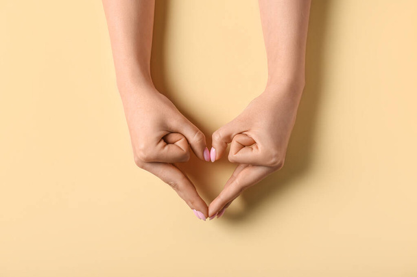 vrouw maken hart met haar handen op beige achtergrond - Foto, afbeelding