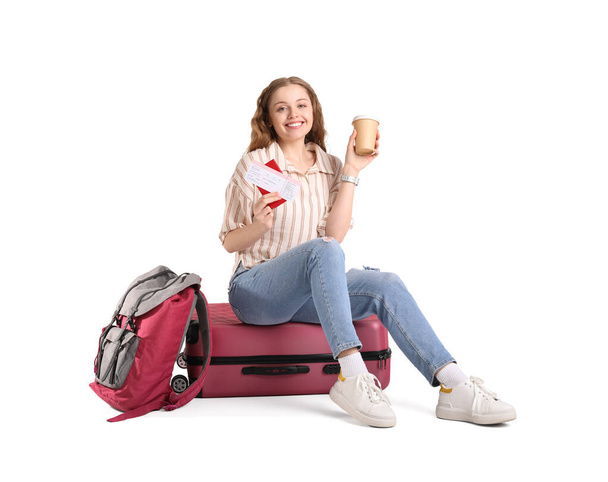 Молодая женщина с чашкой кофе, паспортом и чемоданом на белом фоне - Фото, изображение