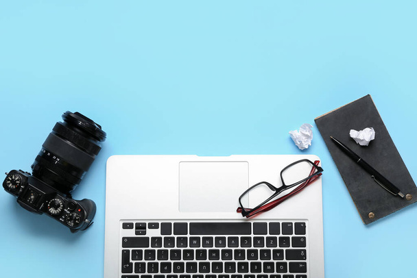 Ноутбук с очками, ноутбуком и фотокамерой на синем фоне - Фото, изображение