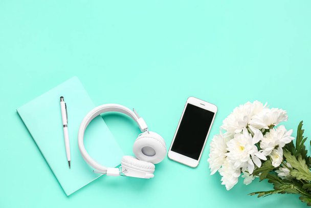 Mobile phone, headphones, notebook and chrysanthemum flowers on color background - Fotó, kép