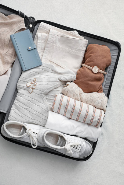 Suitcase with female clothes and accessories on white blanket - Фото, изображение