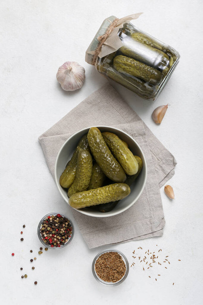 Bowl and jar with tasty fermented cucumbers on light background - Fotó, kép