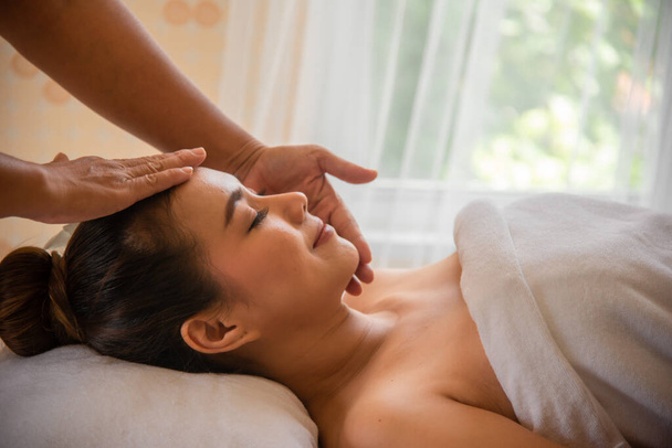 Vista laterale di massaggiatrice professionista facendo massaggio alla testa bella donna asiatica in camera spa. - Foto, immagini