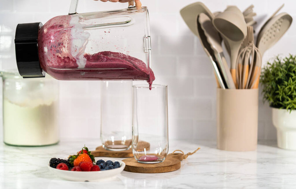 Pouring freshly made mixed berry smoothie into a drinking glass. - 写真・画像