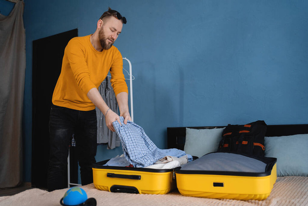 Homme adulte emballant des vêtements dans une valise sur le lit à la maison, se préparant pour le voyage, concept de voyage de vacances. Espace de copie - Photo, image