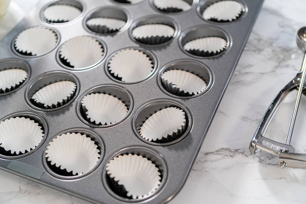 Scooping cupcake beslag met deeg primeur in een bakvorm cupcake pan met liners om mini vanille cupcakes te bakken met ombre roze buttercream glazuur. - Foto, afbeelding