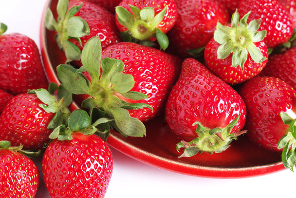 Primer plano de fresas sobre un plato rojo sobre fondo blanco - Foto, imagen