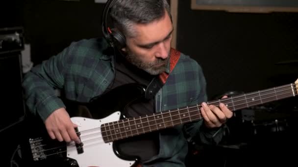 Muzikant die elektrische bas speelt met hoofdtelefoon in de opnamestudio. Muziekproductie. - Video