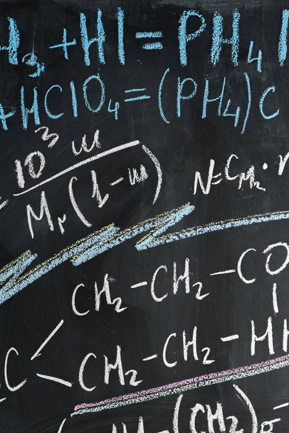 different chemical formulas are written in colored chalk on a black slate wall - Foto, Bild