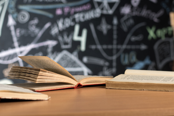 open boeken liggen op een bureau of tafel tegen een krijtbeschilderde schoolbordwand - Foto, afbeelding