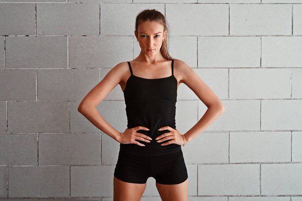 Time to get my fitness on. Cropped portrait of a sporty young woman standing with her hands on her hips against a wall - Fotografie, Obrázek