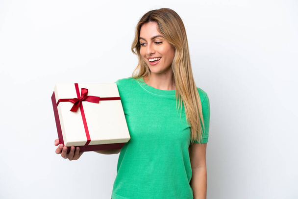 Junge uruguayische Frau hält ein Geschenk auf weißem Hintergrund mit glücklichem Gesichtsausdruck - Foto, Bild