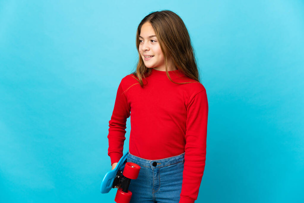 klein meisje over geïsoleerde blauwe achtergrond met een skate - Foto, afbeelding