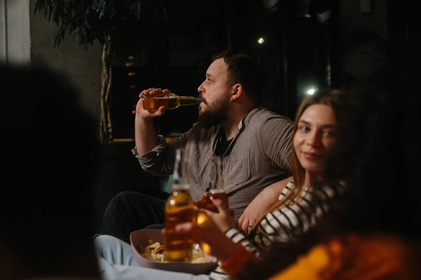 Un grupo de amigos se divierten juntos en un café por la noche, beber cerveza y charlar. - Foto, Imagen