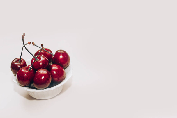 Спелые красные вишни в белых тарелках на столе. - Фото, изображение