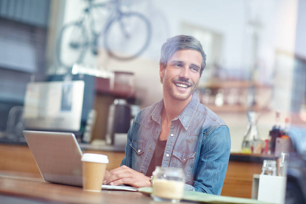 Φρέσκος καφές και δωρεάν Wi-Fi. Ένας όμορφος νεαρός που κάθεται με το λάπτοπ του σε μια καφετέρια. - Φωτογραφία, εικόνα