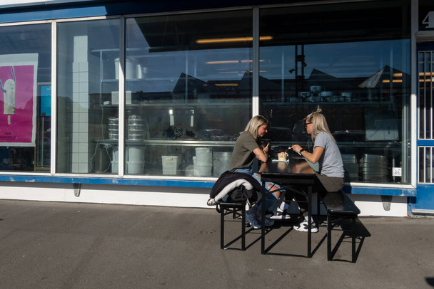 デンマーク・コペンハーゲン旧食肉加工区の春の日差しの中でアイスクリームを食べる屋外レストランに座っている2人の女性. - 写真・画像