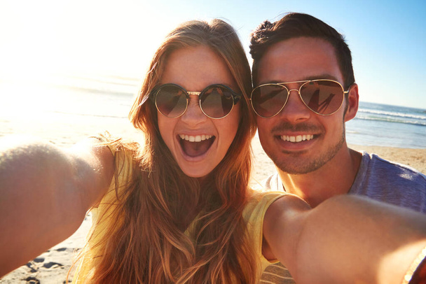 Say cheese. an affectionate young couple taking a selfie on the beach - Фото, изображение