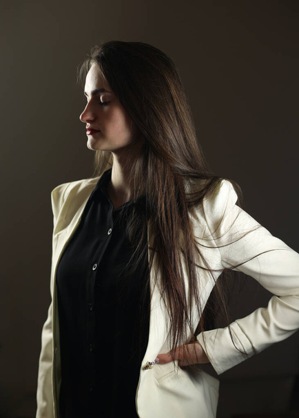Belle fille dans des vêtements élégants. Veste blanche et chemise noire, prise de vue studio. Le modèle pose devant la caméra. - Photo, image