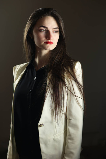 Beautiful girl in stylish clothes. White jacket and black shirt, studio shot. The model poses in front of the camera. - Foto, Imagem