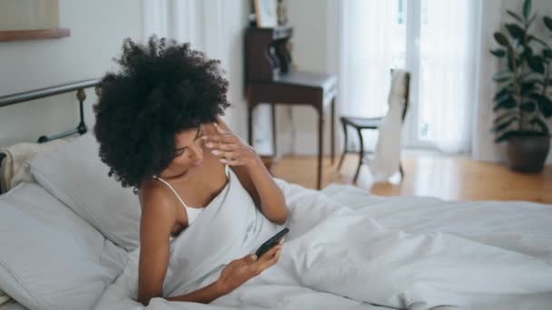 Álmos modell hulló párna kora reggel. Fekete haj álmos hölgy ellenőrzi telefonidő továbbra is alszik puha ágyban. Frusztrált, göndör nő fekszik a hálószobában álmatlanság után. Az időeltolódás fogalma - Felvétel, videó