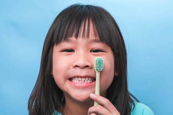 Hymyilevä pieni tyttö, jolla on hammasharja sinisellä pohjalla. Söpö pieni lapsi harjaamassa hampaita. Lasten koulutus suuhygienia, hampaiden reikiintymisen ehkäisy tai hammashoito käsite. - Valokuva, kuva