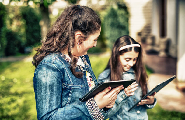 Zwei junge Mädchen mit Tabletten stehen im Stadtpark, - Foto, Bild