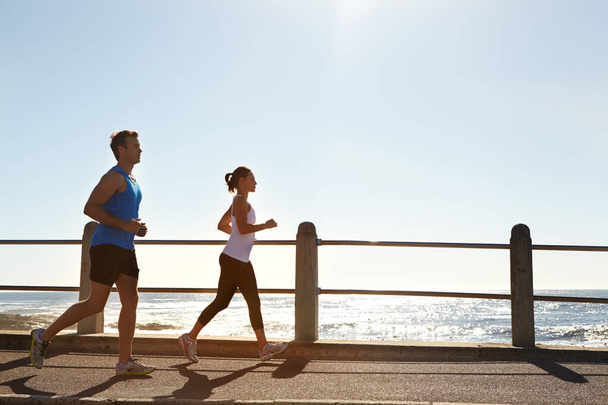 In it for the long run. a young couple jogging together on the promenade - Foto, Imagen