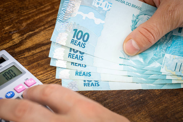Mann hält brasilianisches Geld, Rais, und rechnet mit Ausgaben oder Erträgen Rechner, Finanzkonzept, Eigenheimbudgets in Brasilien - Foto, Bild