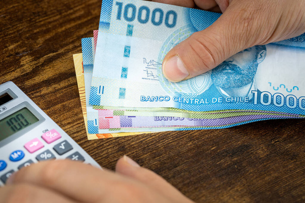 Ένας άνθρωπος κρατά Χιλιανά πέσος στο χέρι του και μετράει τα έξοδα ή τα κέρδη σε μια αριθμομηχανή, Οικονομική έννοια, χιλιανό προϋπολογισμό στο σπίτι - Φωτογραφία, εικόνα