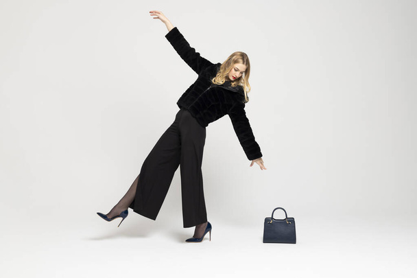 Young Curly blonde girl elegantly dressed, leaning back and reaching her hand to a handbag on the floor. expensive clothes, style and fashion concept. - Photo, Image