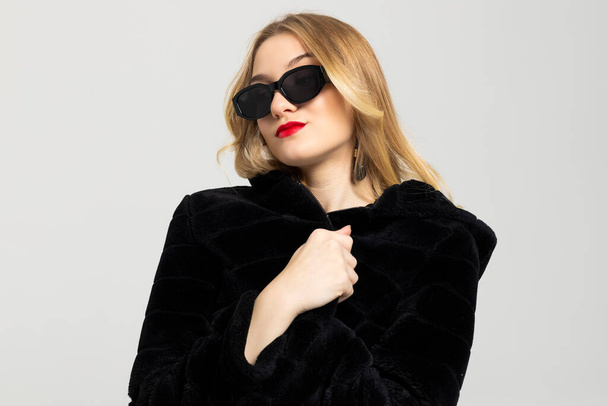 Young Curly blonde girl elegantly dressed, with a bright red lipstick on the lips and a black sunglasses. expensive clothes, style and fashion concept. - Фото, изображение